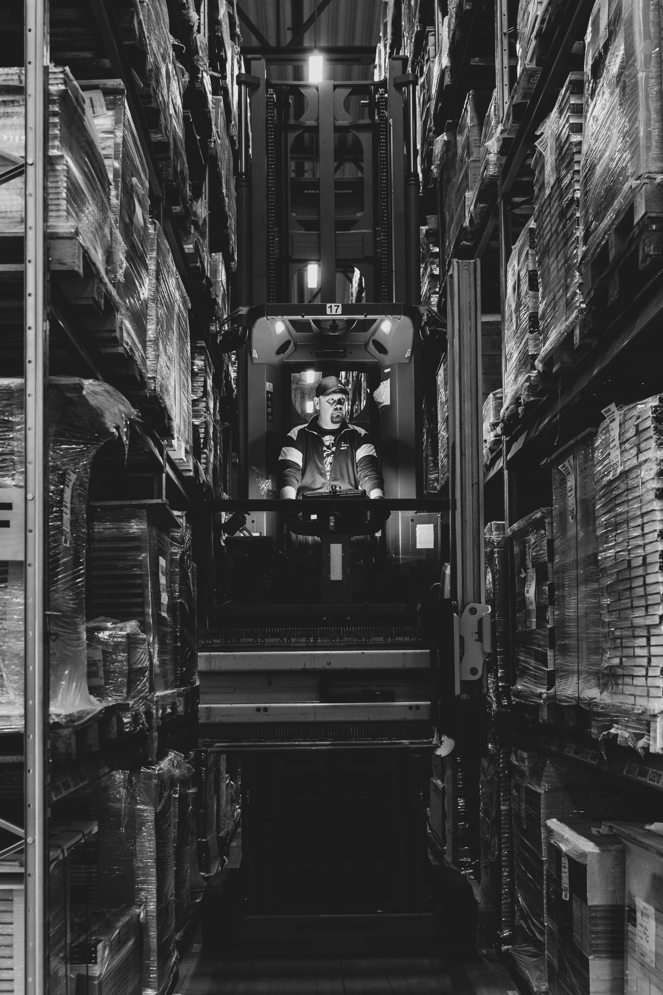 Forklift operator working between tall warehouse racks in a black and white photograph