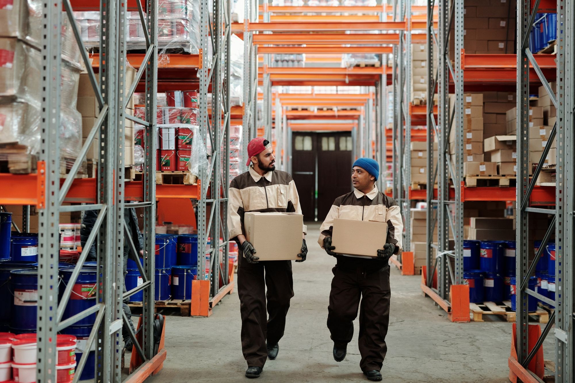 Two warehouse employees carrying boxes through a storage aisle
